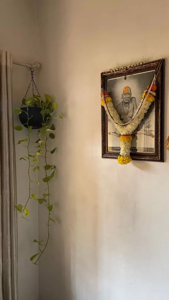 Simple devotional Corner Wall Decor with framed garland, hanging pothos plant in white corner