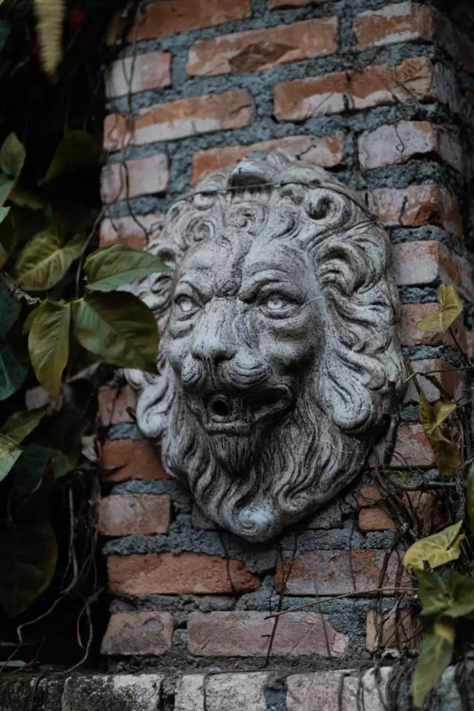 Stone Lion Head Sculpture Mounted On An Ivy Covered Outdoor Brick Wall