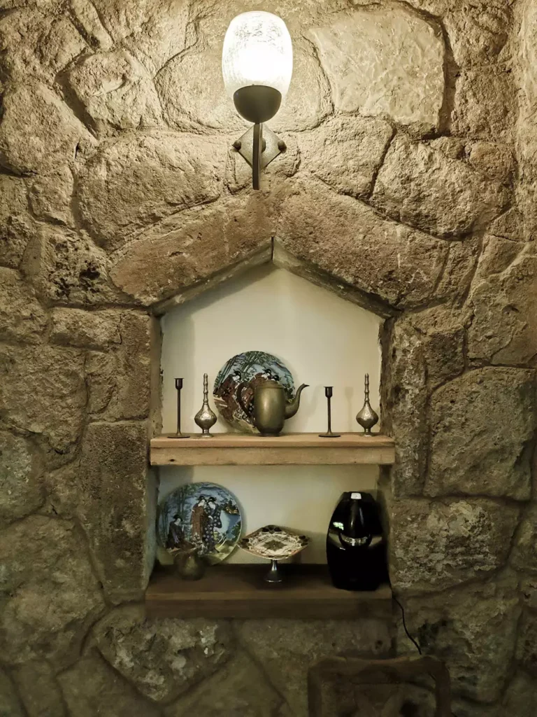 Stone Wall Arch Niche With Brass Teapot And Candlesticks On Wood Shelves