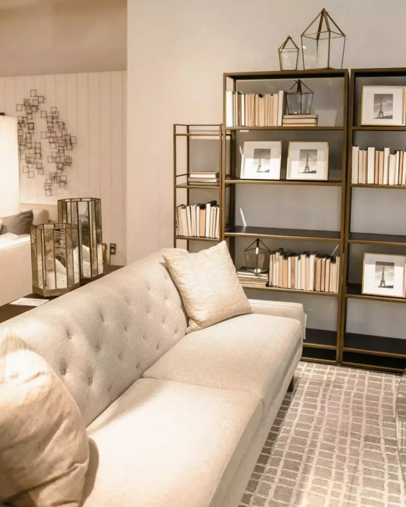 Tan wall living room styled with a tufted beige sofa and a brass bookshelf display
