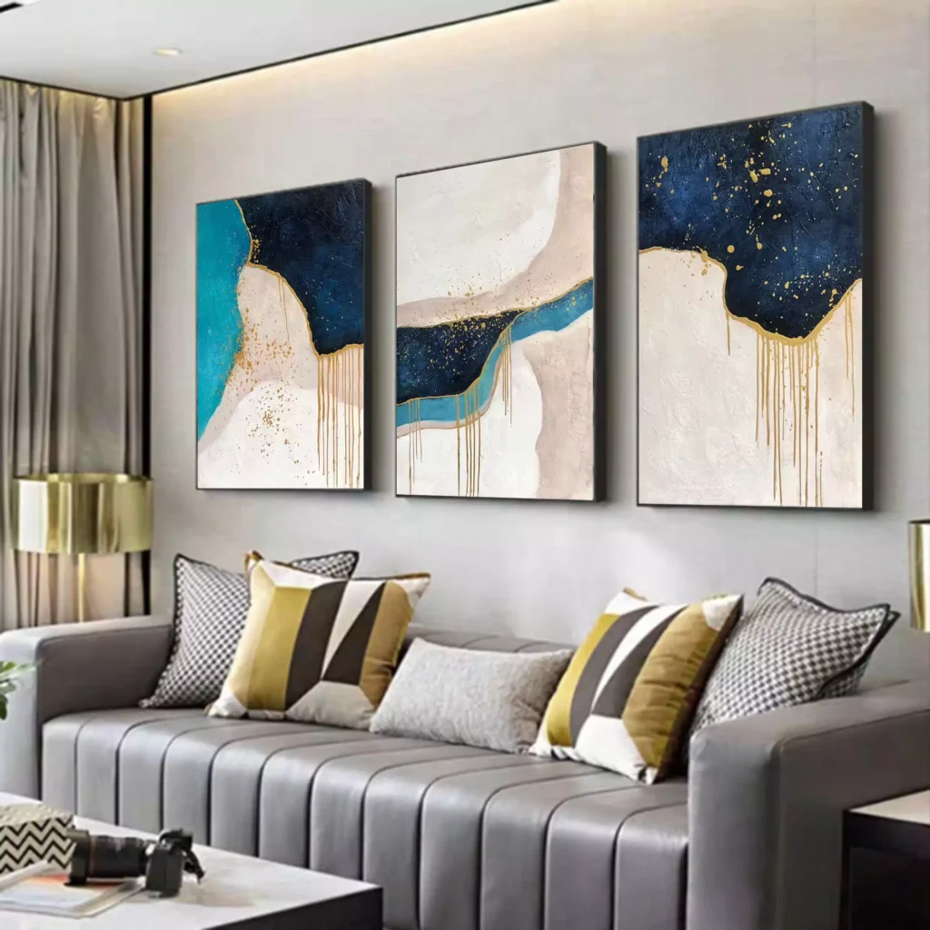 Three-panel abstract blue and gold canvas wall art above gray sofa
