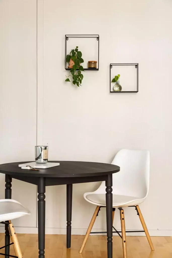 Two black square wall shelves with a philodendron and a small vase keep Dining Wall Decor minimal above a round black table