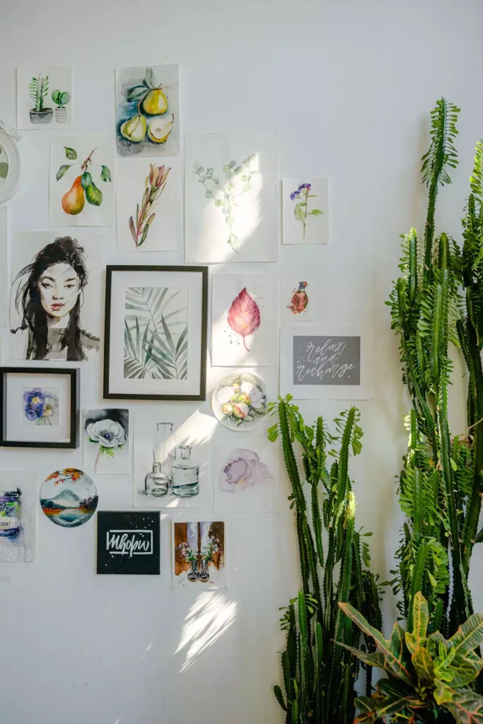 Watercolor illustrations and a portrait forming a gallery wall decoration beside tall cactus plants
