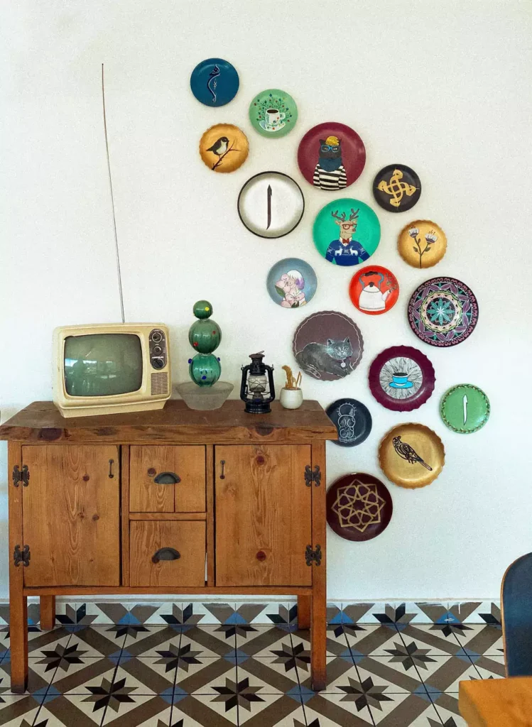Whimsical illustrated plate wall decor arranged in a curved cluster above a vintage TV console