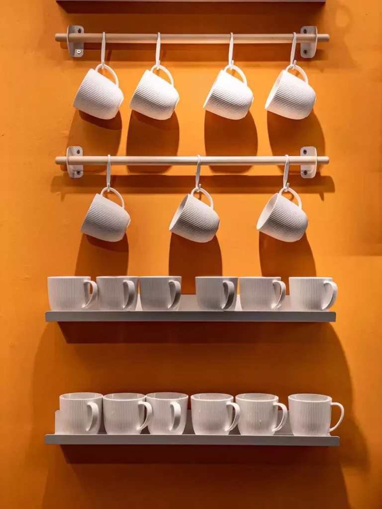 White Mugs Hanging On Rails Against An Orange Wall Make Vibrant Kitchen Wall Decor
