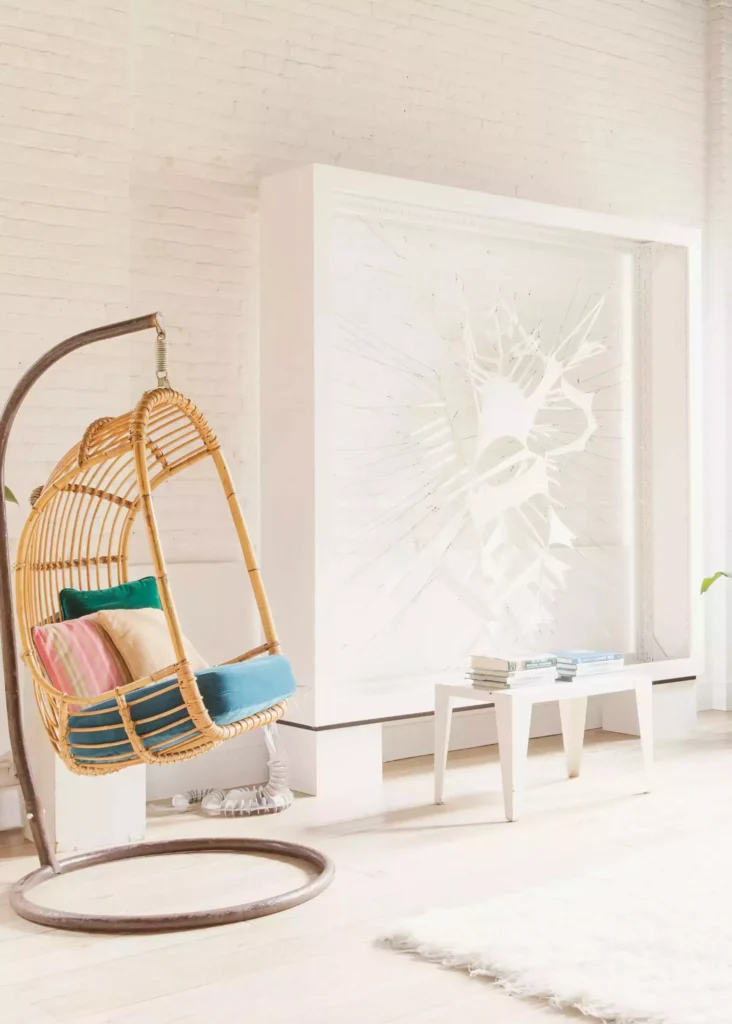 White brick wall, rattan egg chair, oversized framed relief, petite table