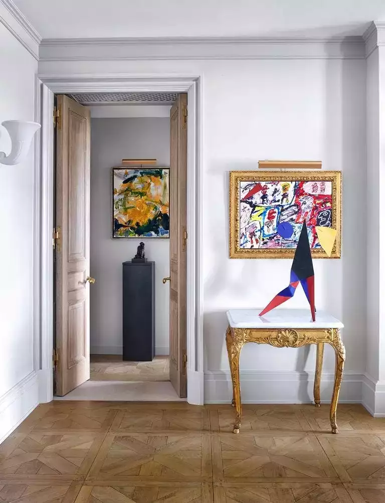 White hallway, gilt console, framed abstract, parquet floor, open double doors