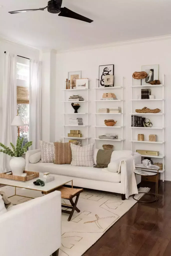 White ladder shelves on a white wall, cream sofa, woven stool, patterned rug