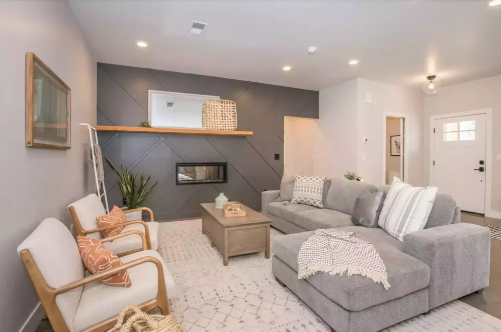 White living room with charcoal herringbone fireplace, gray sectional, wood chairs