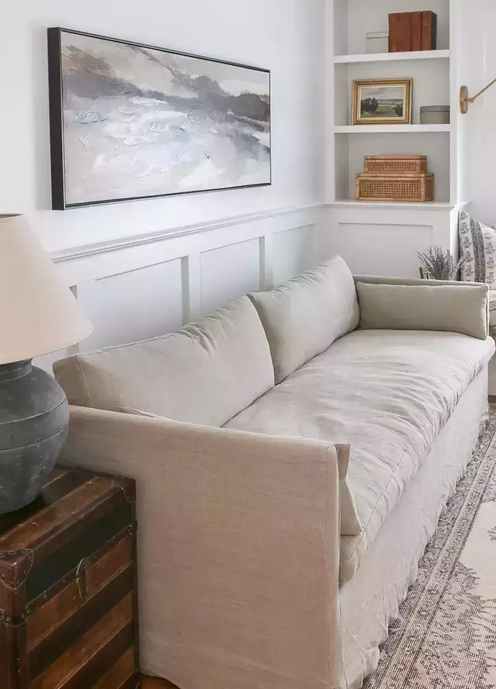 White wainscoting living nook, linen sofa, landscape canvas, vintage trunk