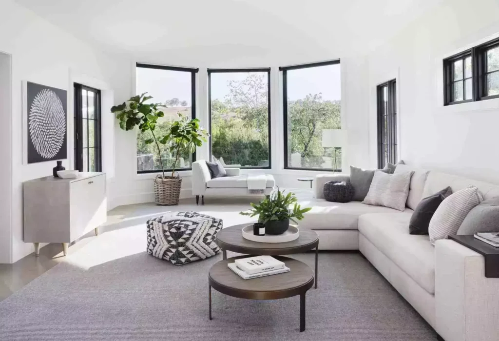 White walls, black-framed bay windows, cream sectional, nested tables, fiddle leaf