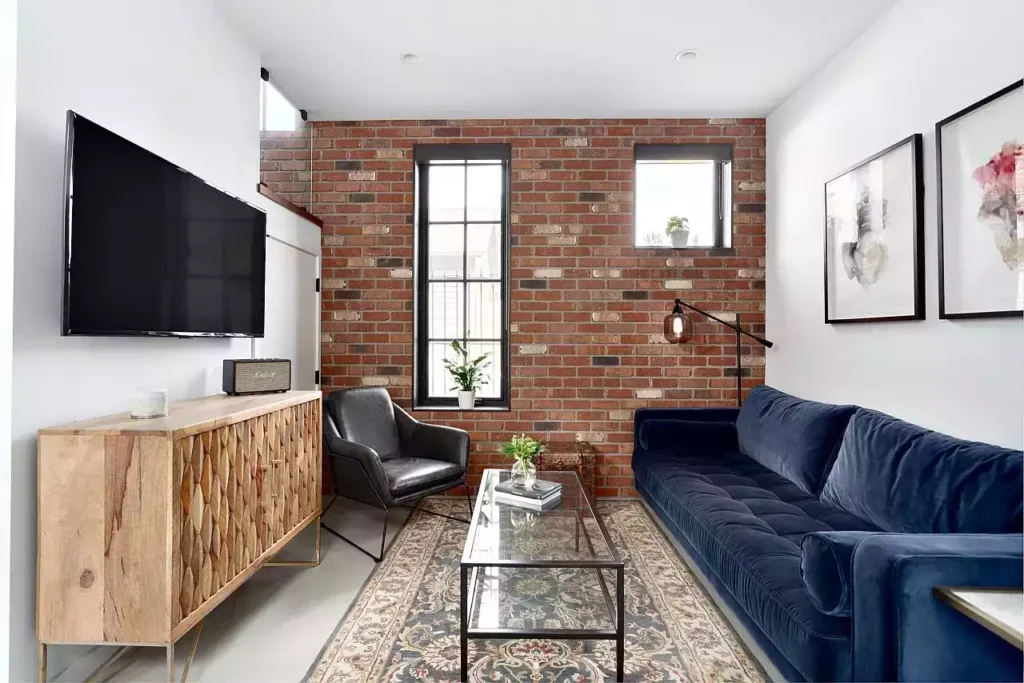 White walls meeting a red brick accent, navy velvet sofa, wood credenza