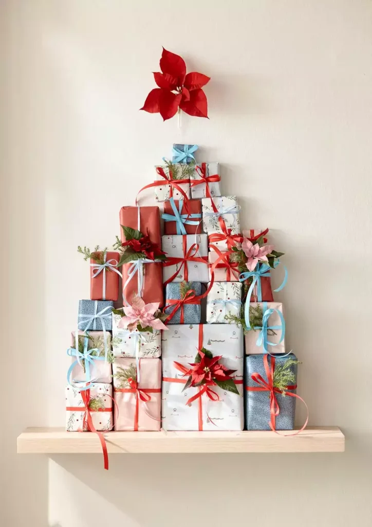 Wrapped Gift Boxes Stacked Into A Christmas Wall Tree Shape On A Shelf, Topped With A Poinsettia Bloom