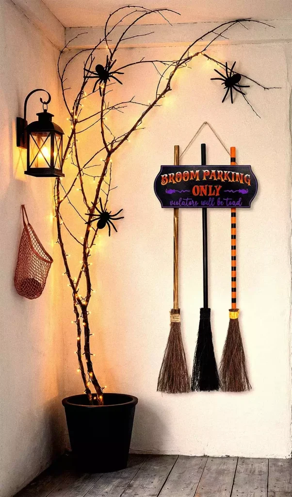 A Broom Parking Only wall sign above three brooms beside a lit bare branch decorated with spiders
