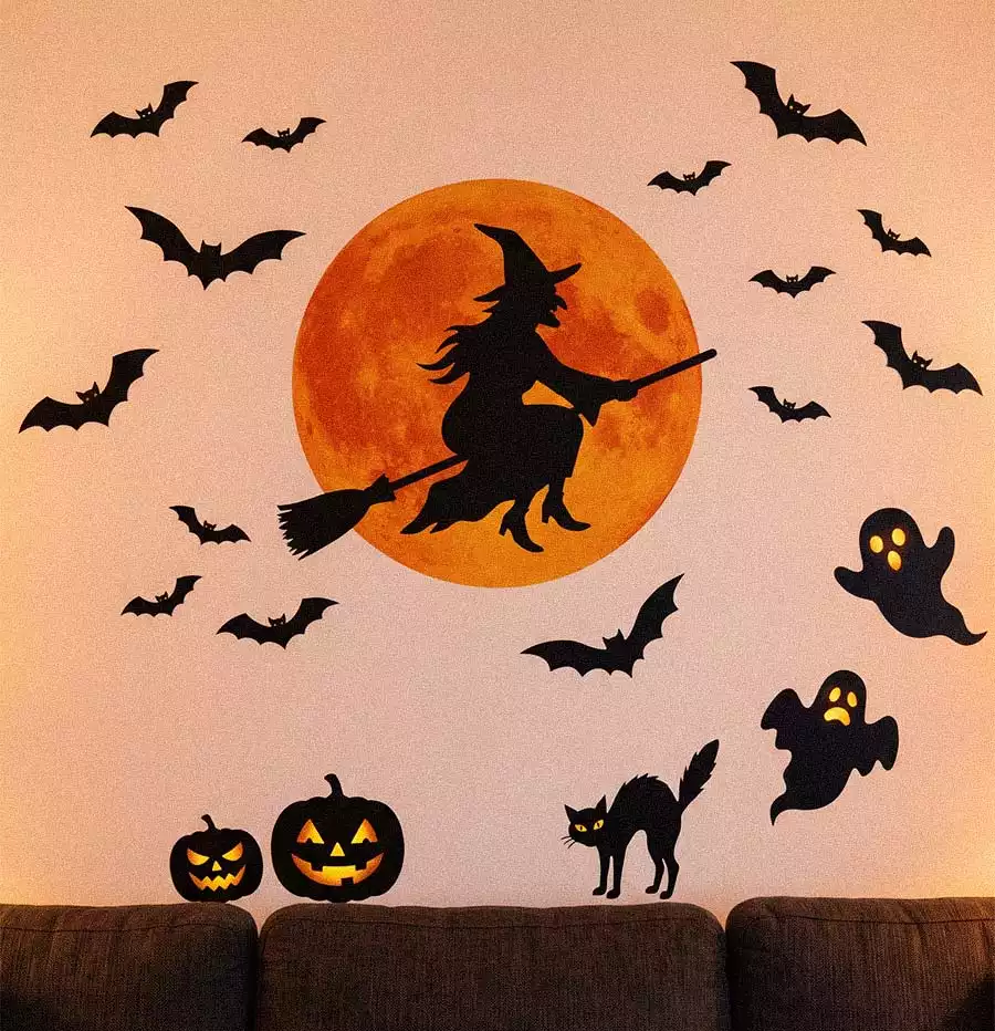 A flying witch silhouette against an orange moon, surrounded by bats, ghosts, pumpkins, and a black cat above a sofa