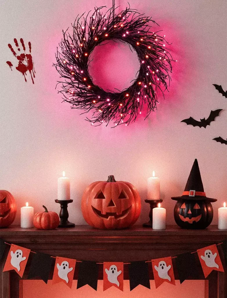 A pink-lit twig wreath above a mantel with jack-o’-lanterns, candles, and a ghost banner