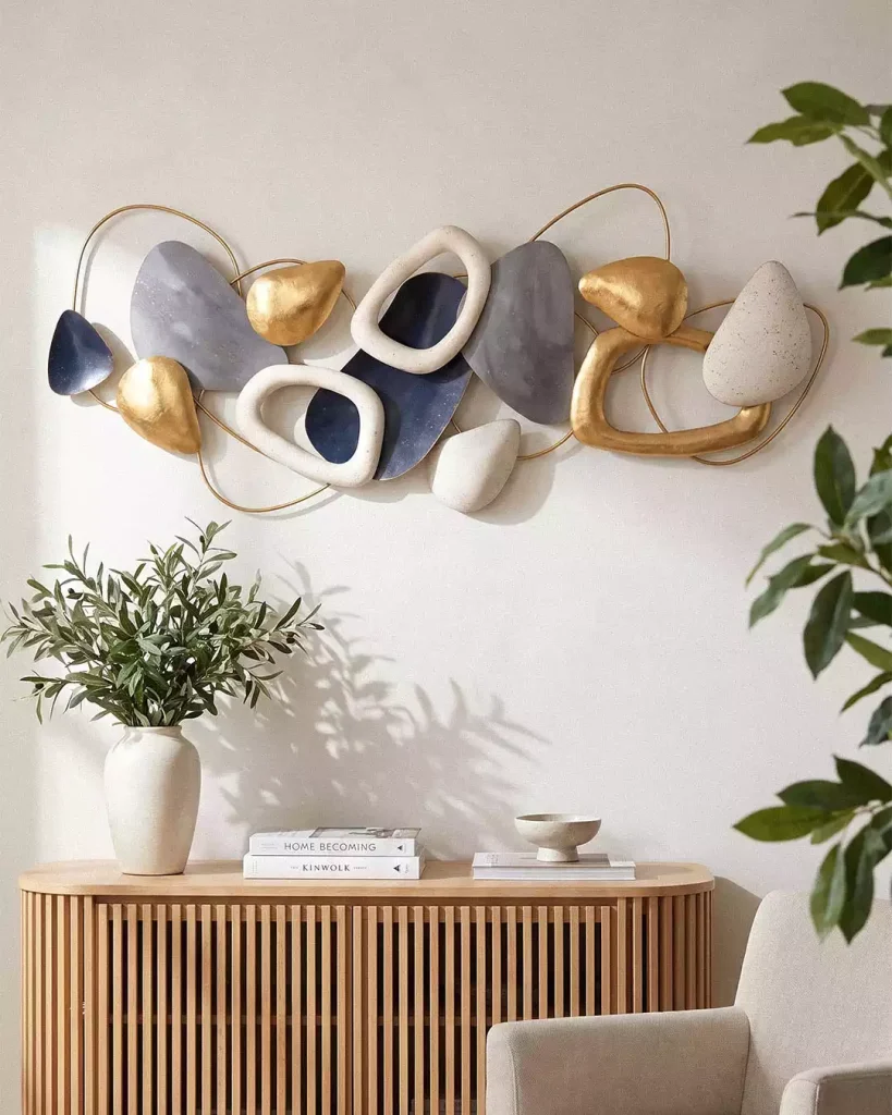 Abstract wall sculpture with gold loops and navy, gray, and cream shapes above a console