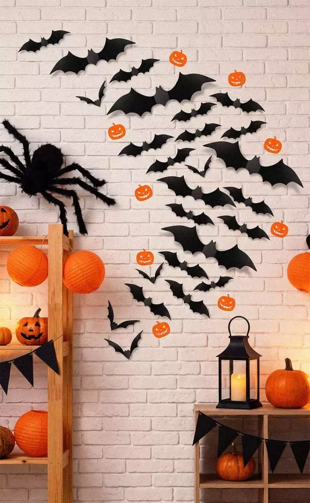 Black bats and orange jack-o’-lantern cutouts sweeping across a white brick wall beside a large spider
