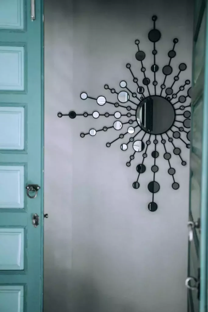 Black sunburst mirror with small circular mirrors beside a turquoise door