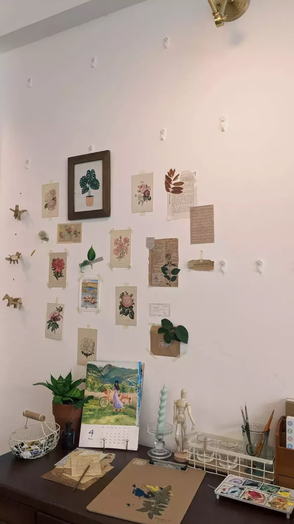 Botanical Pictures Small Cards And Paper Decorations On A Pale Pink Wall Above A Study Desk