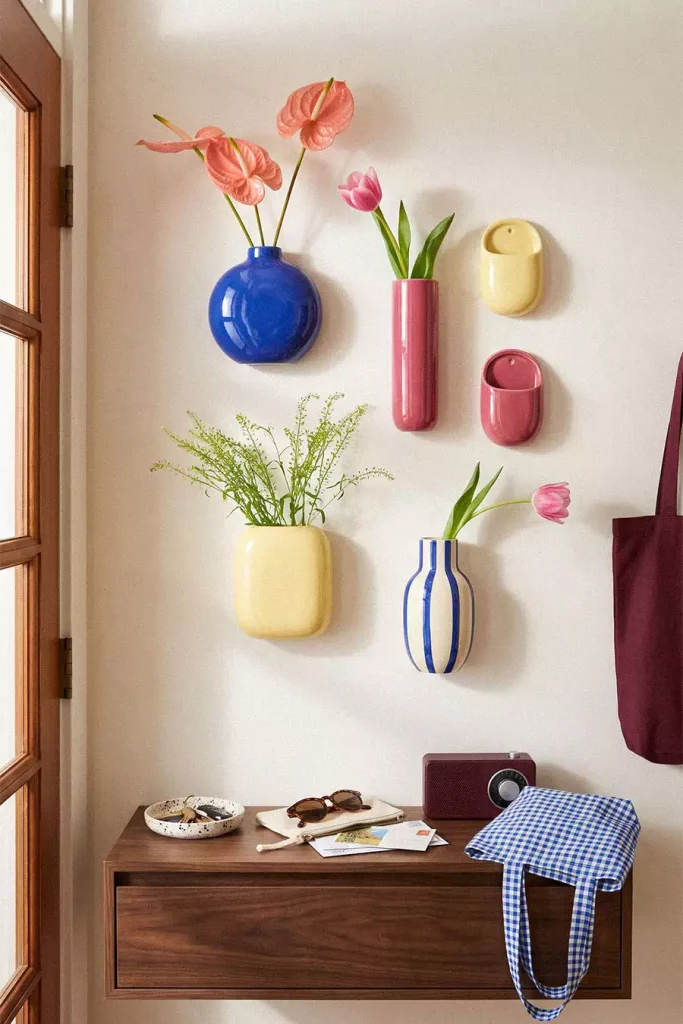 Colorful ceramic wall vases holding flowers and greenery above a walnut console