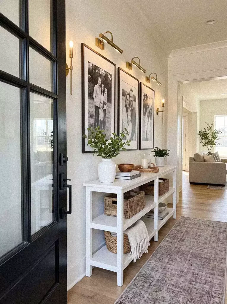 Farmhouse entryway with black and white framed photographs, brass picture lights, and a white console table
