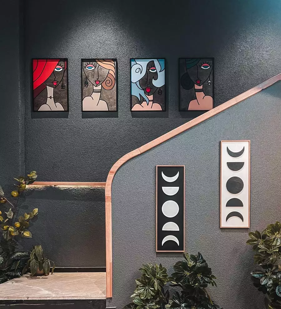 Four colorful stylized portraits hang above a stairway, with two vertical moon-phase prints below a curved wooden handrail