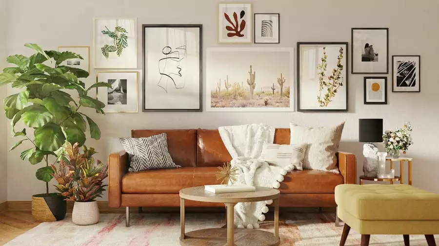 Gallery wall decor combines botanical prints, line drawings, and a desert landscape above a caramel leather sofa beside a large leafy plant