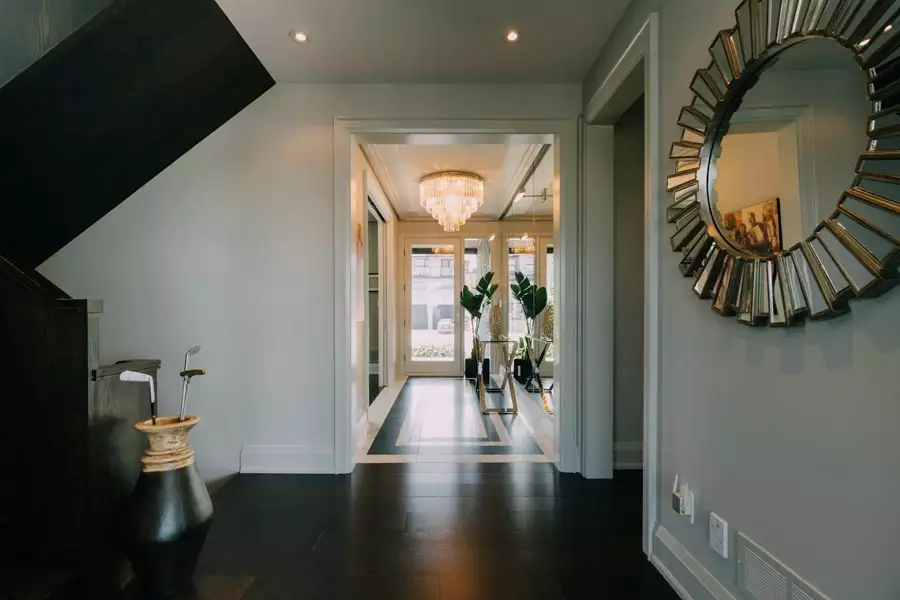 Gray hallway with a decorative segmented round mirror, dark flooring, and a dark staircase