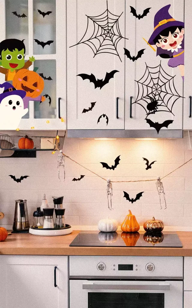 Halloween decals of bats, spiderwebs, a witch, a ghost, and a green monster on white kitchen cabinets