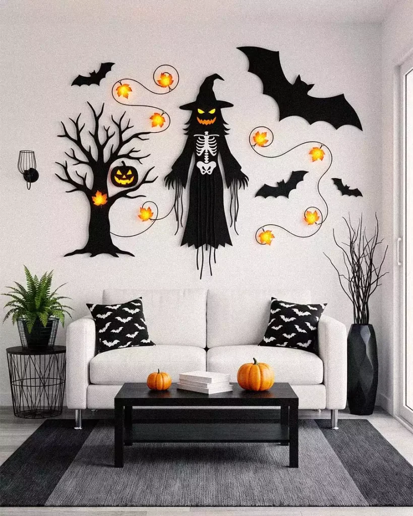 Halloween wall decor with a hanging skeletal witch, bare tree, bats, and orange lights above a white sofa