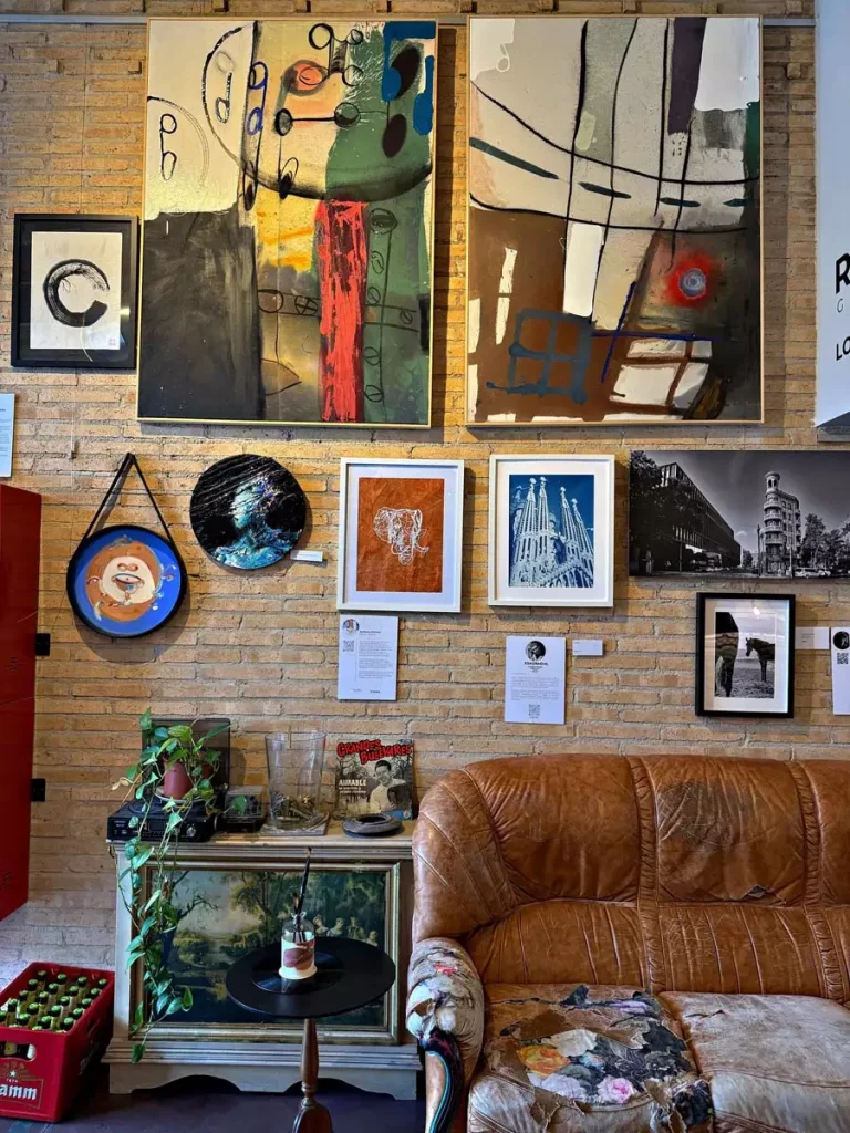 Large abstract paintings, smaller framed artworks, and decorative plates cover an exposed brick wall above a worn brown leather sofa