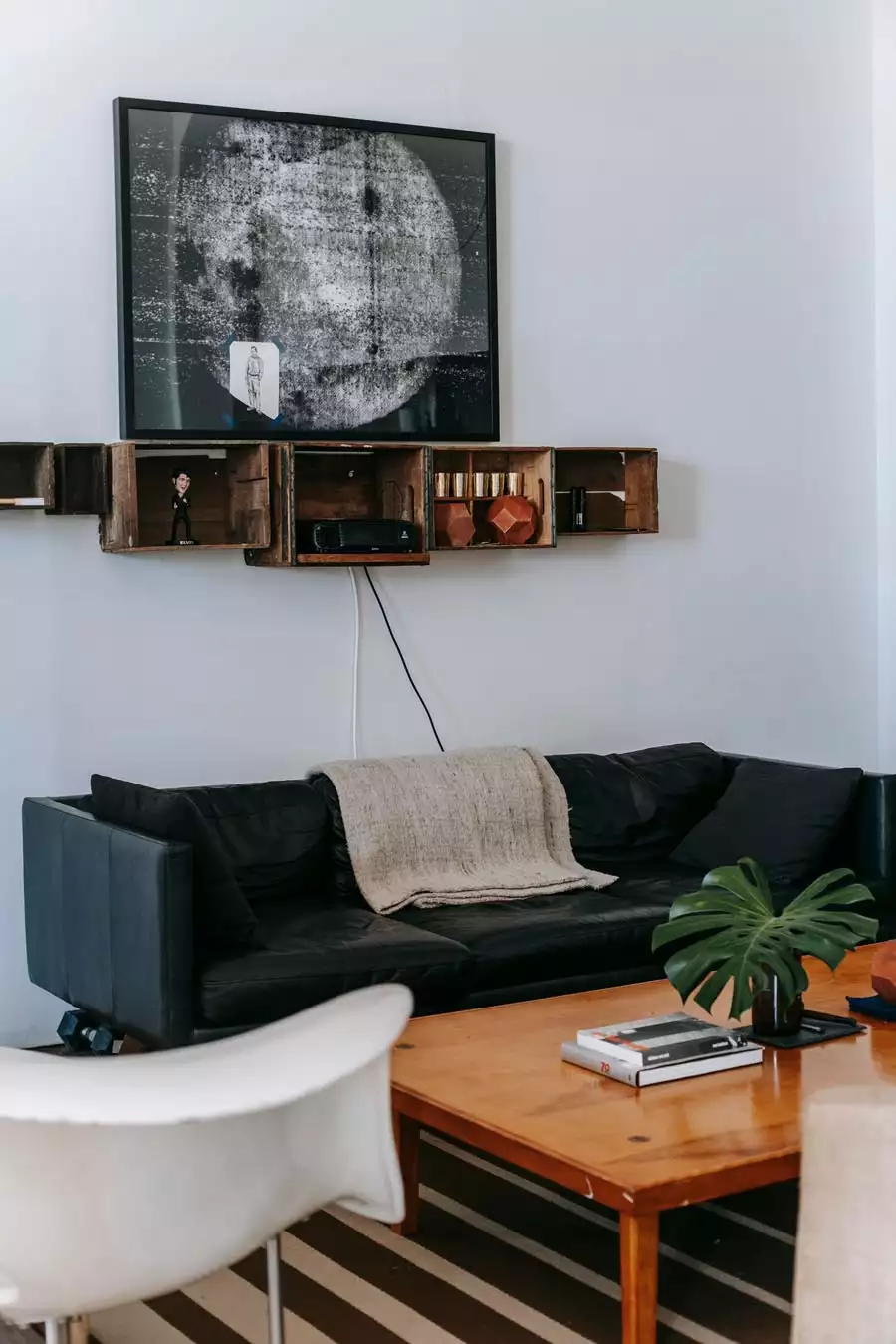 Large monochrome framed artwork above wooden crate shelves and a black sofa