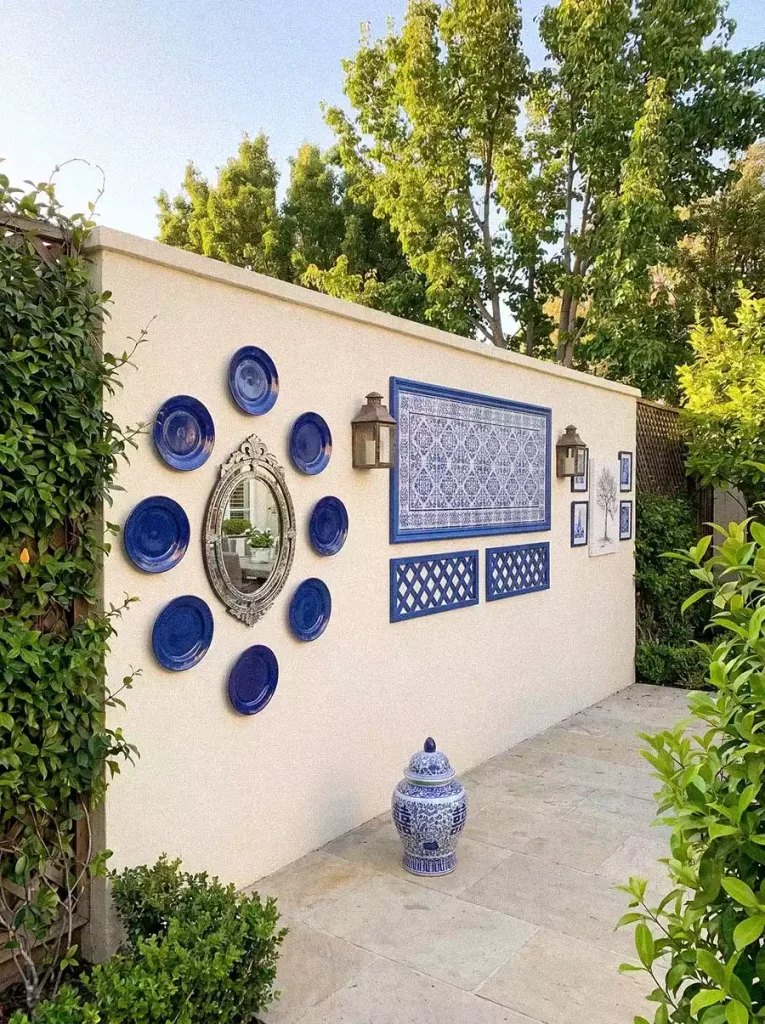 Mediterranean garden wall decor with blue plates around an oval mirror, blue patterned tile panels, and wall lanterns