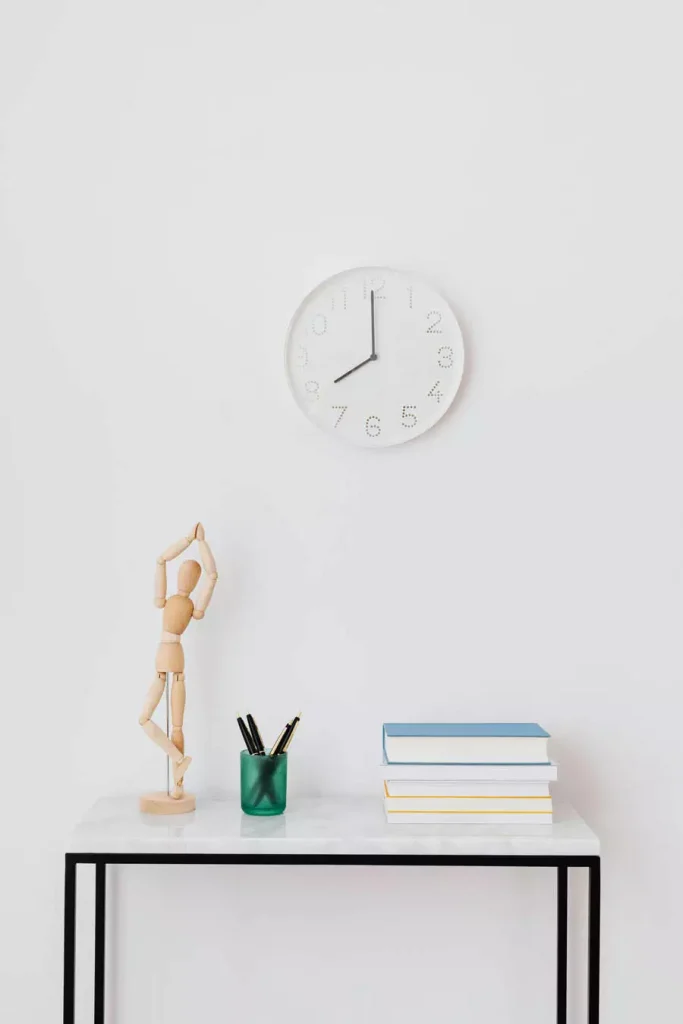 Minimal Study Wall Decor With A White Clock Above A Small Desk Holding Books Pencils And An Artist Mannequin
