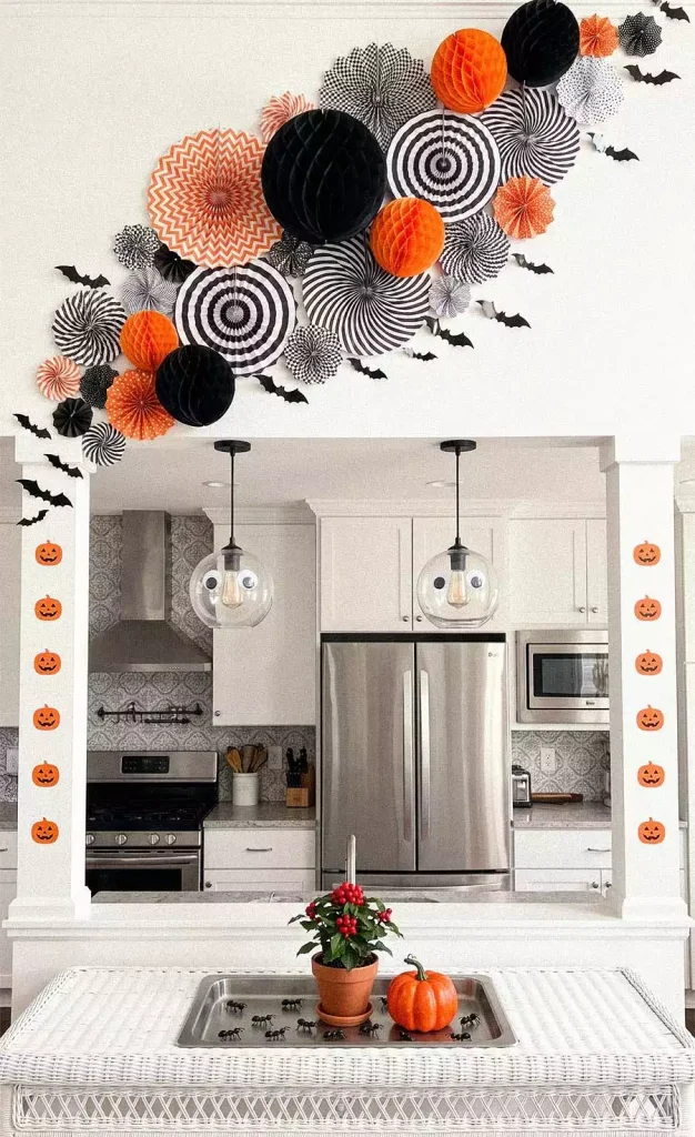 Orange, black, and white paper fans and honeycomb balls arranged above a kitchen opening with bat cutouts