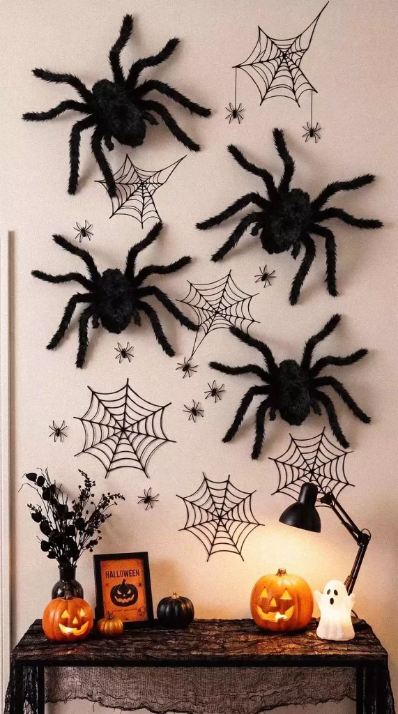 Oversized black spiders and spiderwebs arranged above a console with glowing pumpkins and a ghost ornament