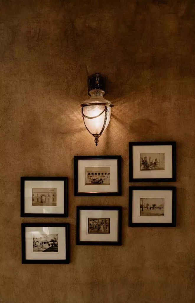 Six black-framed vintage photographs with cream mats hang beneath a glowing lantern on a textured brown wall