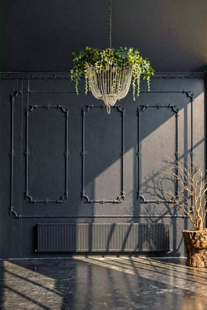 Sunlit ornate raised molding on a charcoal wall beneath a chandelier decorated with greenery