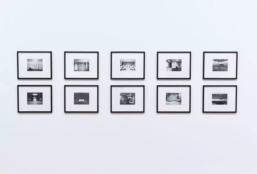 Ten matching black frames with wide white mats display monochrome photographs in two evenly spaced rows on a white wall