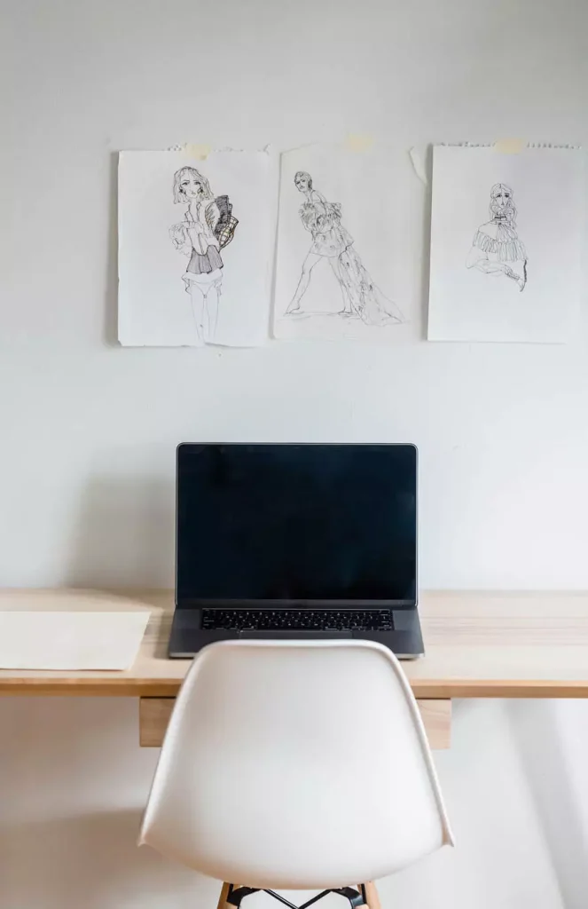Three Unframed Figure Sketches Taped To A White Study Wall Above A Laptop Desk And White Chair