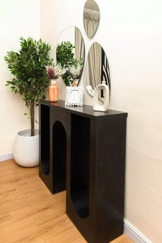 Three oval mirrors arranged above a sculptural black console with decorative vases and a leafy potted tree