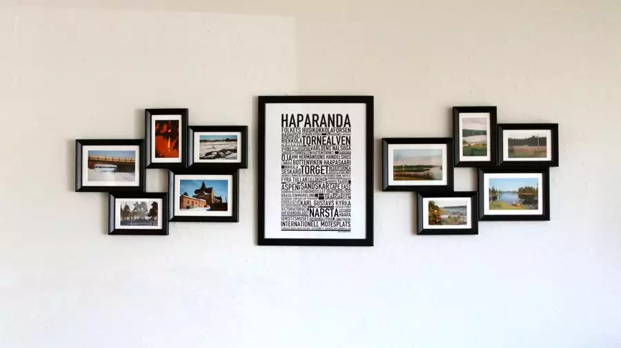 Two clusters of small black-framed photographs flank a large central typography poster on a white wall