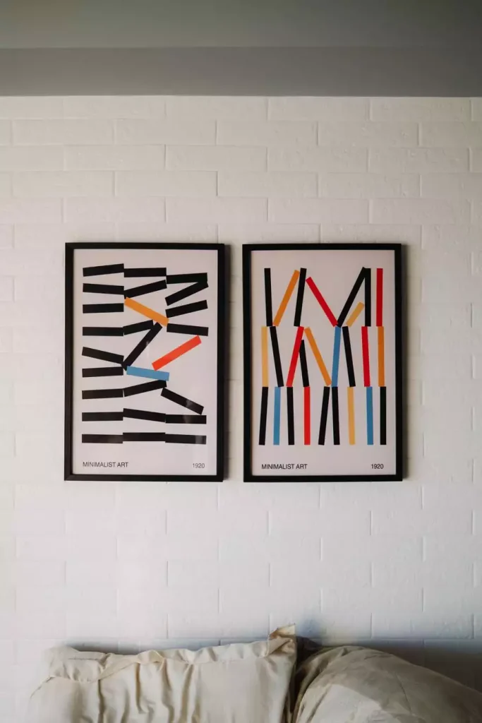Two framed geometric prints with colorful bars on a white brick wall