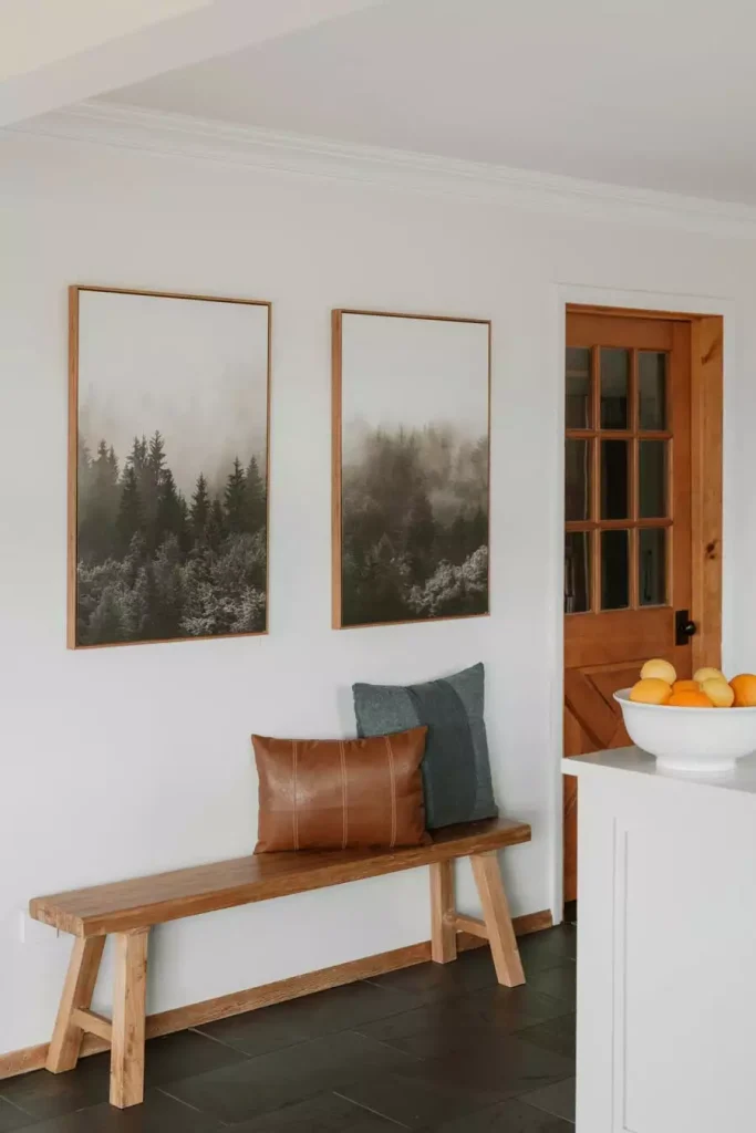Two framed misty forest prints above a simple wooden bench with brown and blue gray cushions