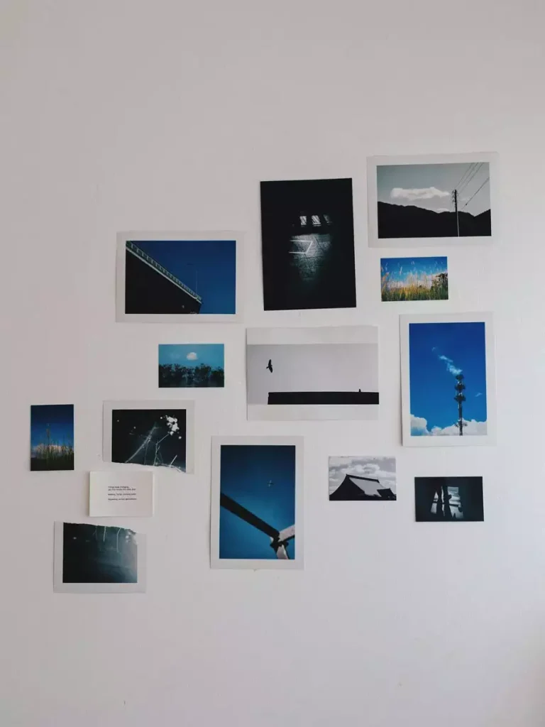 Unframed photographs of blue skies, landscapes, and architectural details form an irregular collage on a pale wall