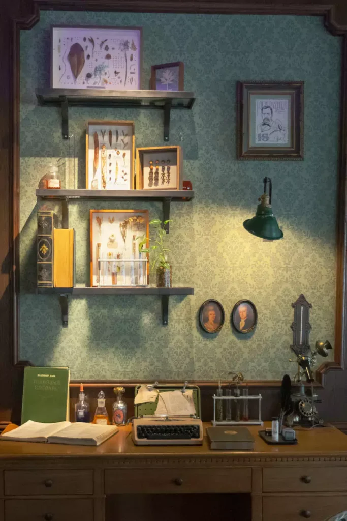 Vintage Study Wall With Patterned Wallpaper Framed Illustrations And Small Shelves Above A Desk With A Typewriter