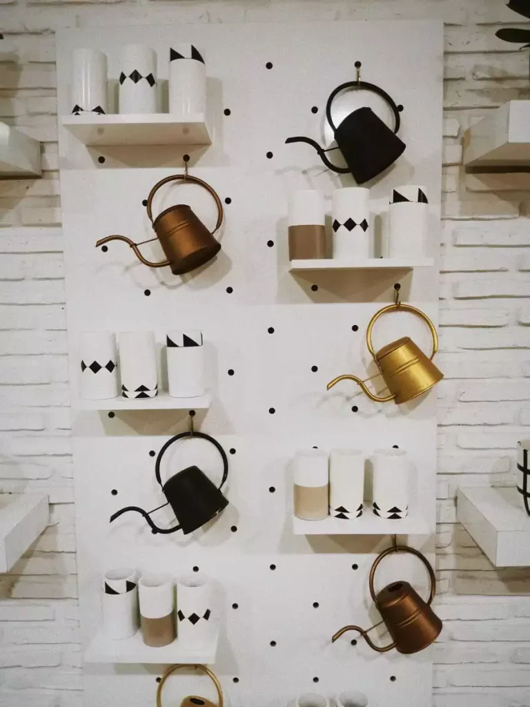 White pegboard wall display with metallic watering cans and patterned pots on shelves