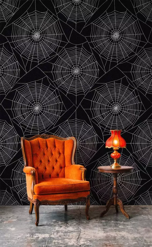 White spiderweb patterns covering a black wall behind an orange velvet armchair and a glowing vintage lamp