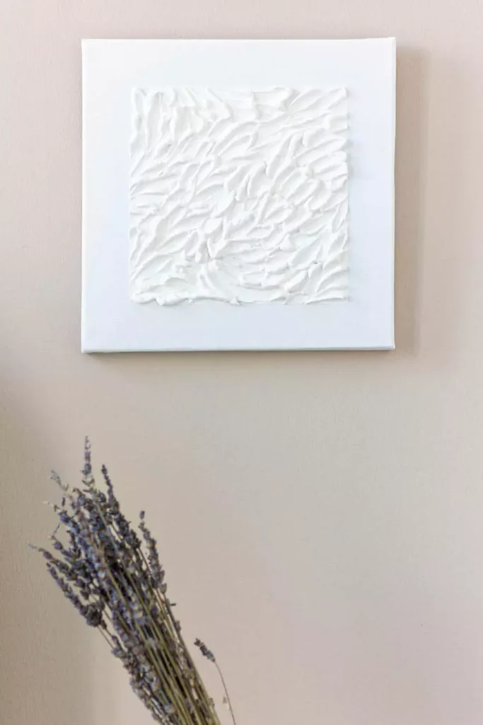 White textured relief artwork above dried lavender against a beige wall